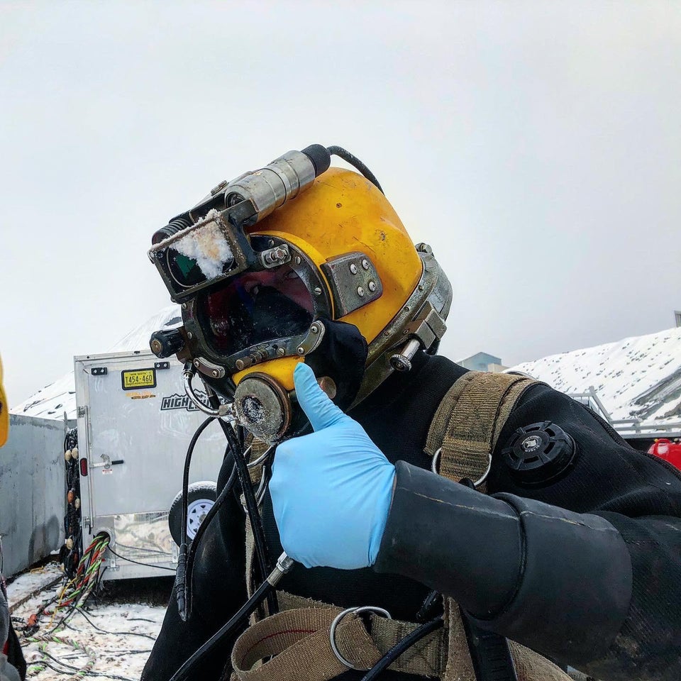 A commercial diver giving the thumbs up. He is wearing his full equipment.