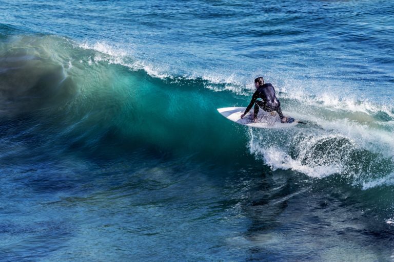 A man wearing a wetsuit is surfing. We want to know what are the differences; diving wetsuit vs surfing wetsuit?